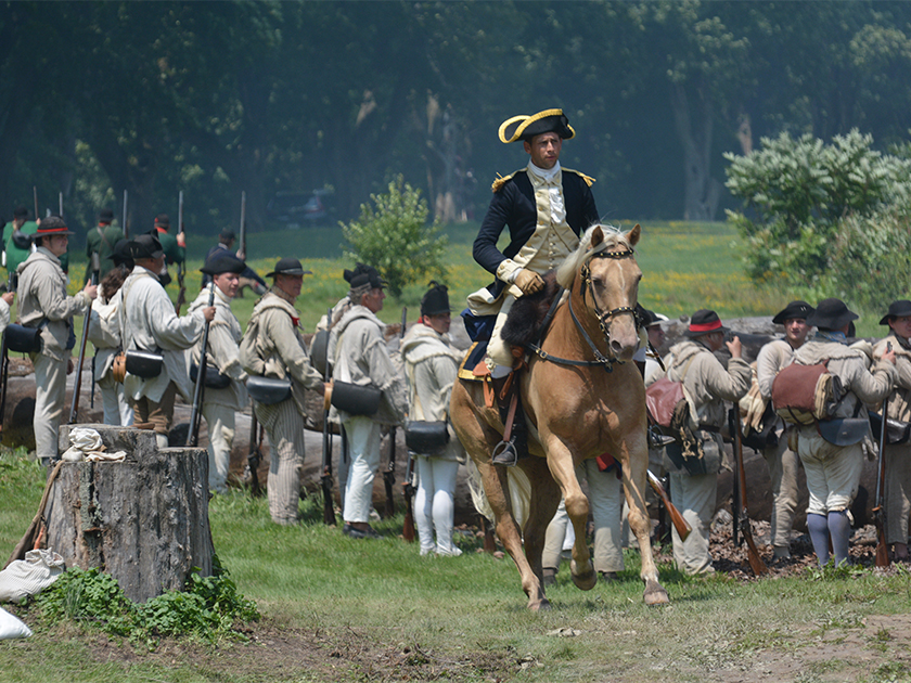 A Revolutionary War reenactor riding a horse, commanding a line of infantry