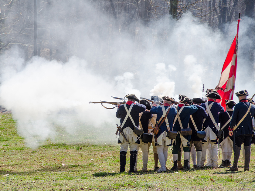 A row of Revolutionary War reenactors firing their muskets in a field