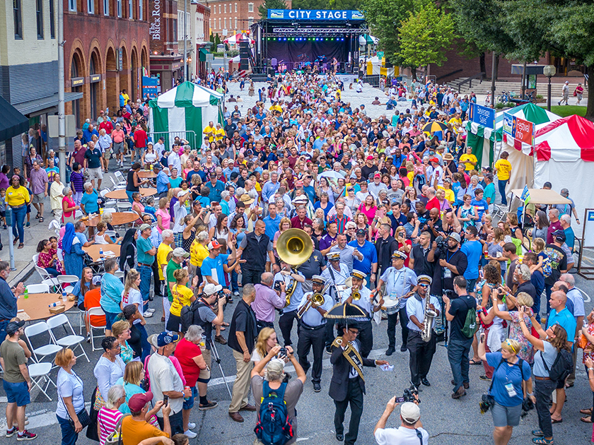 A town street filled with people being led by a second line-style brass band