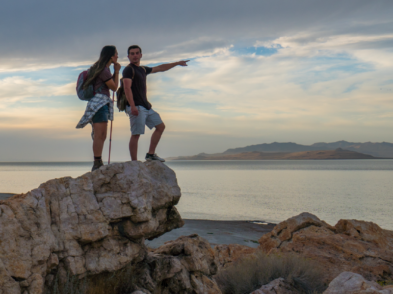 A man and a woman standing on top of a rock overlooking a lake, while the man points into the distance